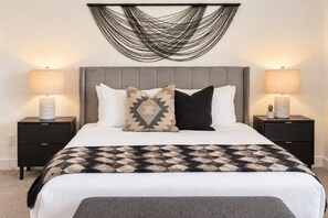 A bedroom with a bed, two bedside tables, a wall-mounted light fixture, and a patterned throw blanket. - The Cardinal | Ultimate Group Retreat in Glendale (Glendale)