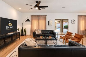A modern living room with a black leather sofa, a coffee table, a TV, and a ceiling fan. - The Cardinal | Ultimate Group Retreat in Glendale (Glendale)