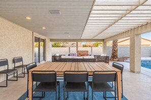An outdoor patio with a wooden table and chairs, a seating area with cushions, and a view of a swimming pool. - The Cardinal | Ultimate Group Retreat in Glendale (Glendale)