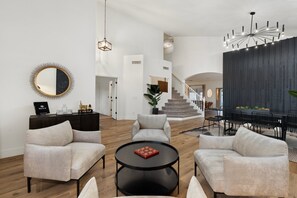 Amplia sala de estar con un espejo redondo, dos sillones, una mesa de centro, una escalera y un comedor con una lámpara moderna.