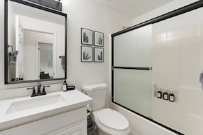 A bathroom with a white sink, a toilet, a shower with a glass door, and framed botanical prints on the wall.