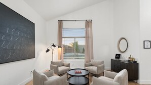 A modern living room with a large blackboard, a round coffee table, four armchairs, a floor lamp, a window with blinds, a dark wooden cabinet, and a mirror on the wall. - The Cardinal | Ultimate Group Retreat in Glendale (Glendale)