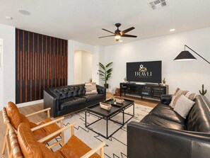 A modern living room with a black leather sofa, a wooden coffee table, and a television on a black stand. - The Cardinal | Ultimate Group Retreat in Glendale (Glendale)
