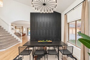 Uma área de jantar moderna com parede de destaque em madeira escura, uma escada e vista através de grandes janelas.