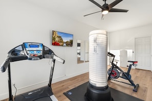 A home gym with a treadmill, stationary bike, punching bag, and a TV displaying a cityscape.
