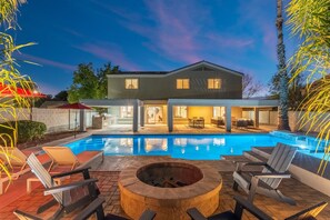Una casa moderna con piscina, zona de estar exterior y una fogata.