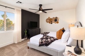 A modern bedroom with a bed, a ceiling fan, a TV, a wall art piece, and a window with blinds. - The Cardinal | Ultimate Group Retreat in Glendale (Glendale)