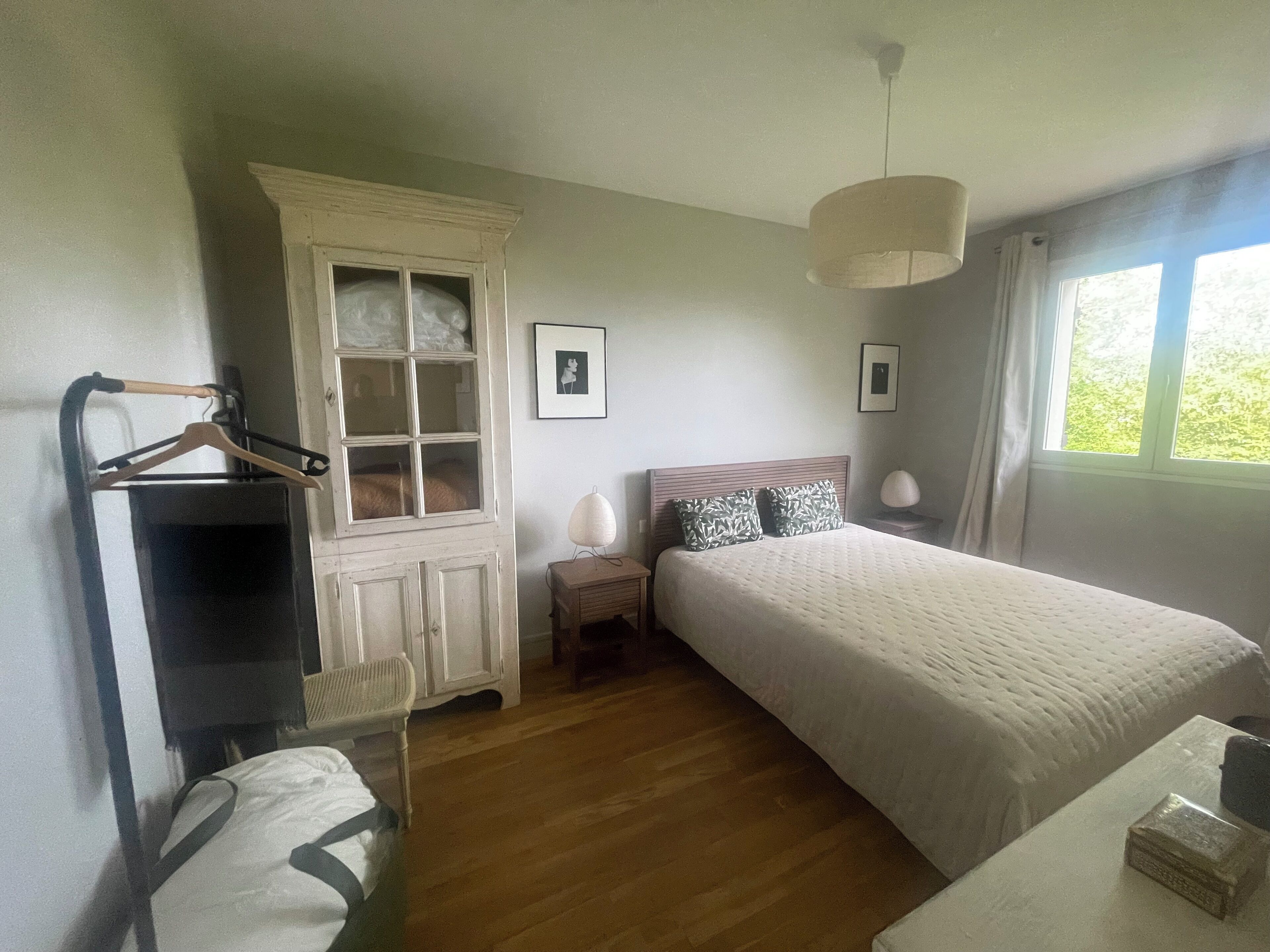 Un dormitorio con cama, armario, mesita de noche y ventana.