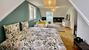 A bedroom with a sloped ceiling, a bed with floral bedding, a hanging light fixture, and a window with a view of the outdoors. - Renovated country property with fireplace, near forest (Le Mont-Saint-Adrien)
