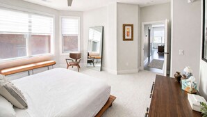 Ein Schlafzimmer mit einem großen Bett, einem Schreibtisch, einem Stuhl, einem Deckenventilator und einer Tür zu einem anderen Raum.