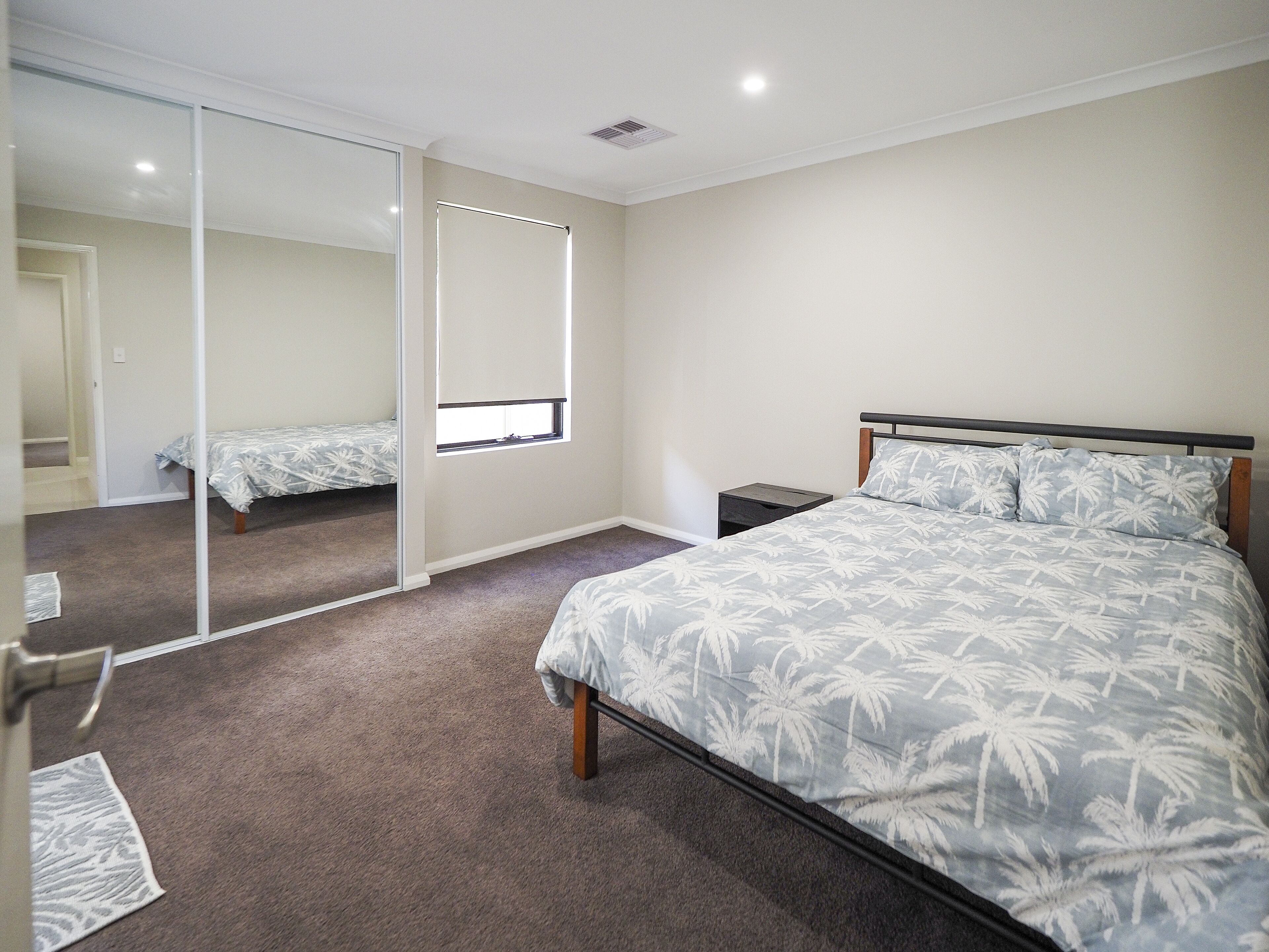 Une chambre à coucher avec un grand lit, une table de chevet, un miroir et une porte coulissante donnant sur une autre pièce.