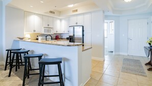 Une cuisine moderne avec des meubles blancs, un îlot central doté de tabourets, un réfrigérateur et un four à micro-ondes.