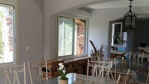 A dining area with a glass table and white chairs, a brick fireplace, and a wooden ceiling beam. - CHARMING HOUSE WITH PRIVATE POOL (Prunelli-di-Fiumorbo)