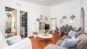 A living room with a sofa, a coffee table, and a TV. There is a dining area with chairs and a table.