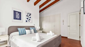 A neatly made bed with white linens and two pillows, a bedside table with a lamp, and a wall with two framed artworks.