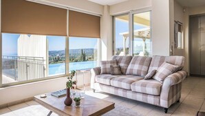 A modern living room with a checkered sofa, large windows with blinds, a wooden coffee table, and a view of a balcony and landscape.