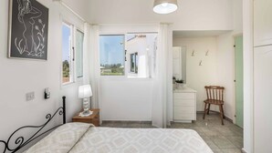 Un dormitorio con cama, una mesita de noche con lámpara, una silla, un escritorio con espejo y una ventana con cortinas.