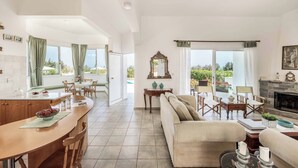 Amplia sala de estar con sofá, mesa de comedor y chimenea. Un ventanal grande ofrece vistas al exterior.