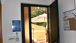A doorway leading to an outdoor area with a sandy ground, a bench, and a large umbrella.