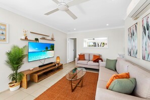 Ein modernes Wohnzimmer mit Flachbildfernseher, Deckenventilator, Sofa, Couchtisch und einer Topfpflanze.