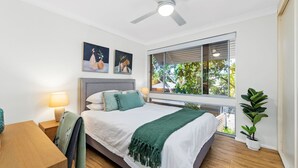 A bedroom with a bed, a window with blinds, a ceiling fan, and a nightstand with a lamp.