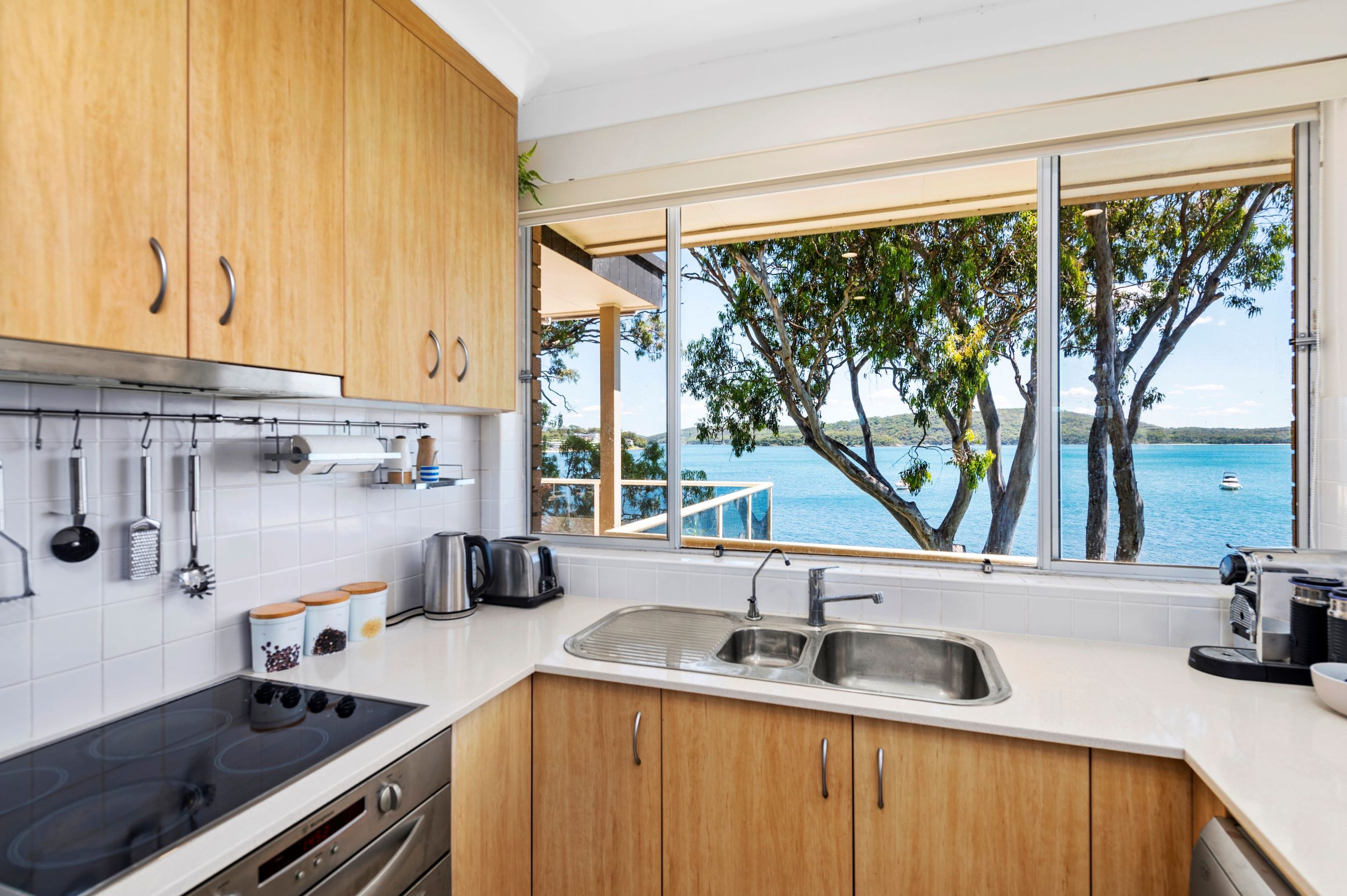 A modern kitchen with wooden cabinets, a stainless steel sink, and a view of the sea through large windows.
