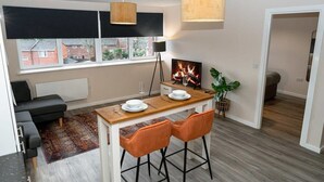A modern kitchen with a dining table, two orange chairs, a black sofa, a wooden floor, and a view of the outside. - Modern & Spacious 1 Bed Apartment in Manchester (Salford)