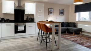 A modern kitchen with white cabinets, a black stove, and a dining area with a table and two chairs. - Modern & Spacious 1 Bed Apartment in Manchester (Salford)