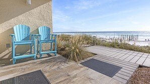 Une terrasse en bois avec deux chaises Adirondack bleues, une vue sur la plage et un ciel dégagé.