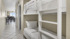 Une chambre avec des lits superposés, un coin repas avec des chaises et une vue sur l’extérieur.