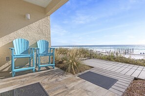 A wooden deck with two blue Adirondack chairs, a view of the beach, and a clear sky.