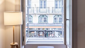 Ein Zimmer mit Holzboden, einer Bank, einer Lampe und einem Fenster mit Blick auf ein Gebäude mit Balkonen.