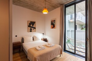 A bedroom with a bed, a nightstand, a lamp, and a large window with a view of a balcony.