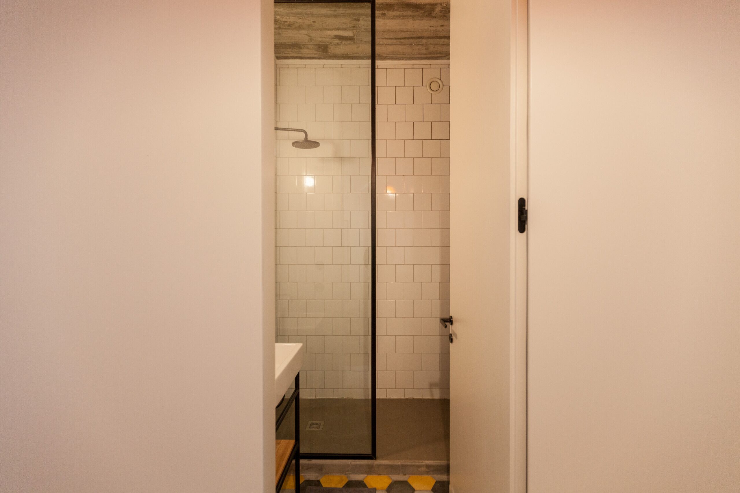 A modern bathroom with a glass shower enclosure, white tiled walls, and a wooden floor.
