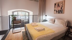 A bedroom with a bed, a chair, a balcony with a plant, and a painting on the wall.
