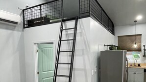 A loft bedroom with a ladder leading to a mezzanine, a kitchenette, and a bathroom.