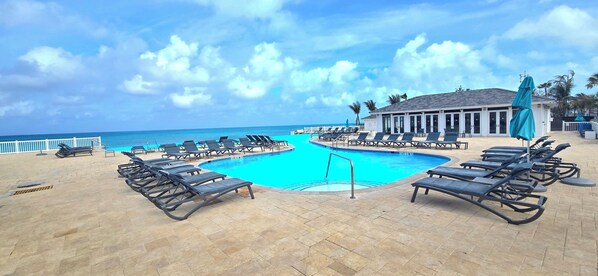 A pool area with lounge chairs, a pool, and a building with large windows.