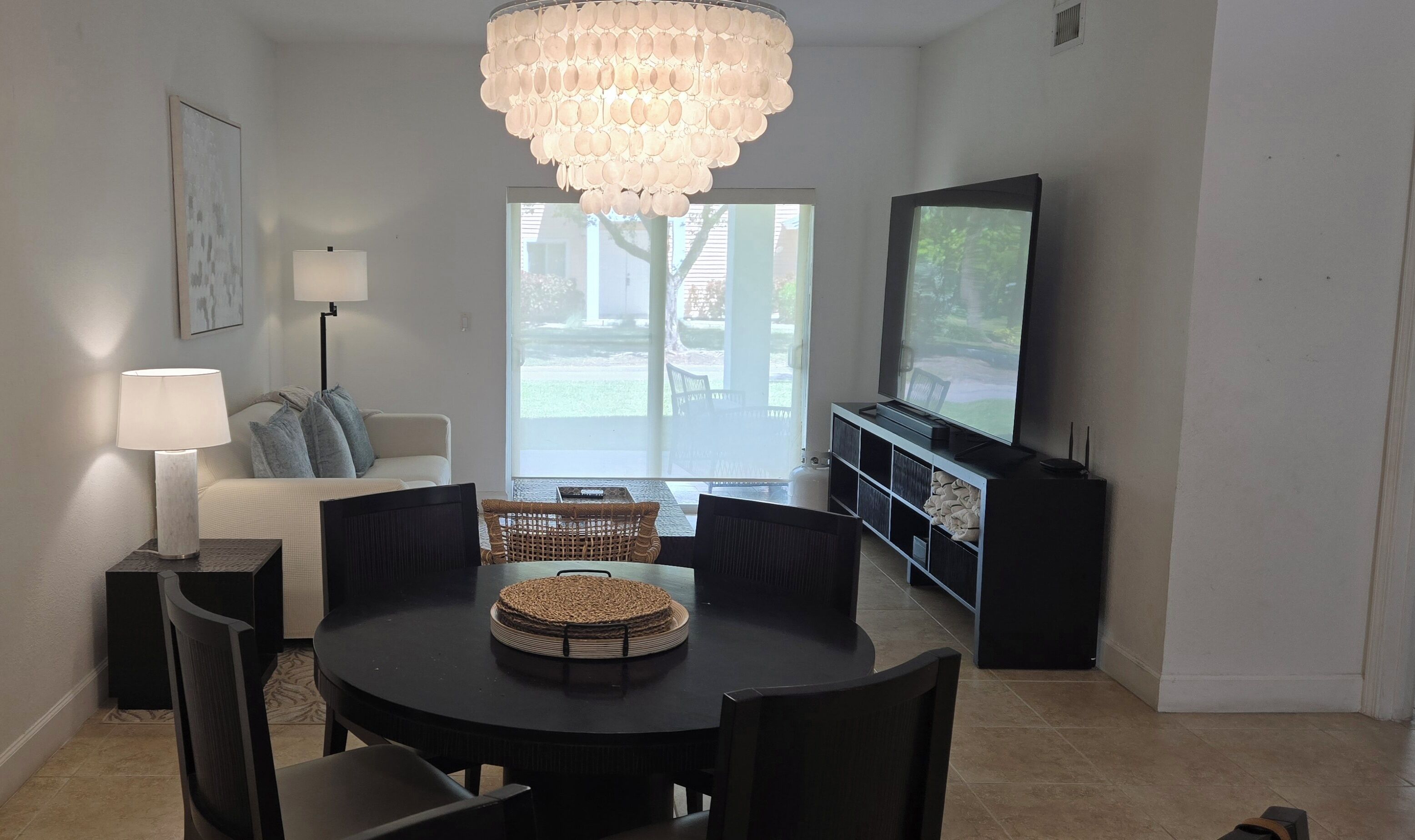 Un espace repas comprenant une table ronde, des chaises, un lustre, un canapé, un téléviseur et une porte-fenêtre coulissante.
