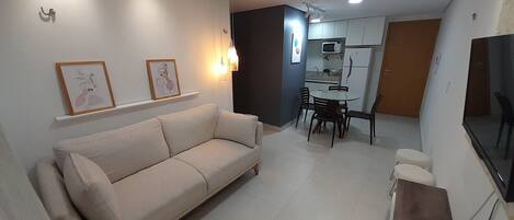 A living room with a sofa, a dining table with chairs, a TV, and a kitchen area with cabinets and a microwave.