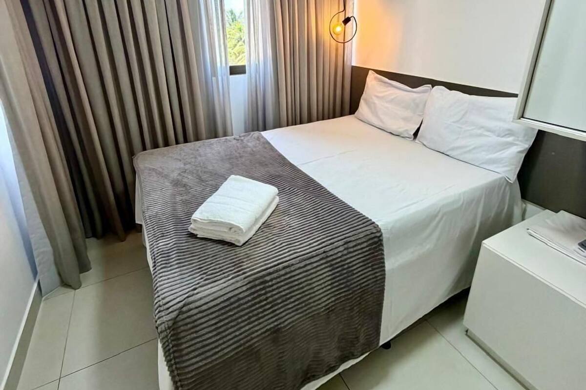 Ein Hotelzimmer mit einem Bett, einem Nachttisch, einer Lampe und Vorhängen.