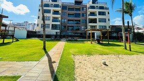 Un edificio de varios pisos con un patio central, palmeras y una zona arenosa.