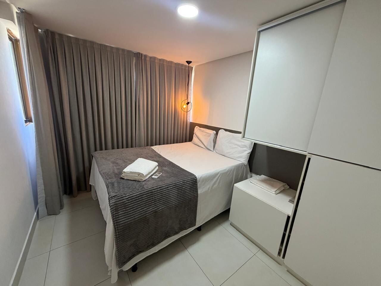Ein Hotelzimmer mit Bett, Nachttisch, Schrank und einem Fenster mit Vorhängen.
