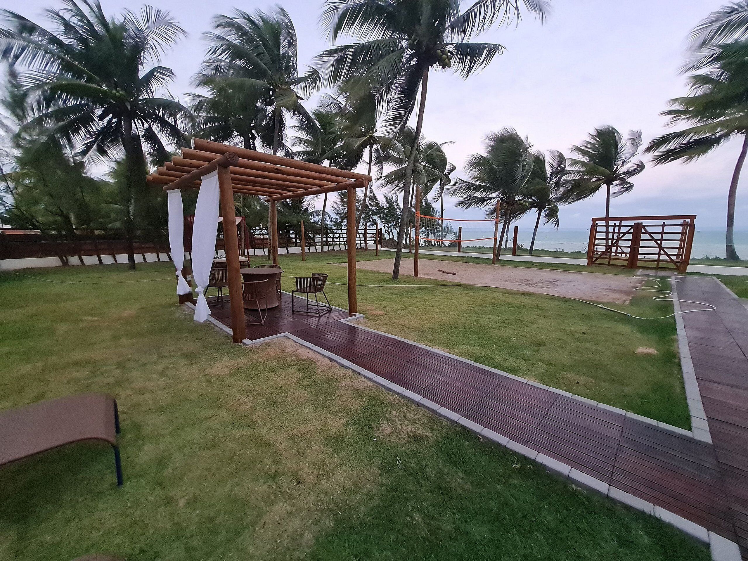 Un espacio de estar al aire libre cubierto con una pérgola, una red de voleibol y vista al mar.