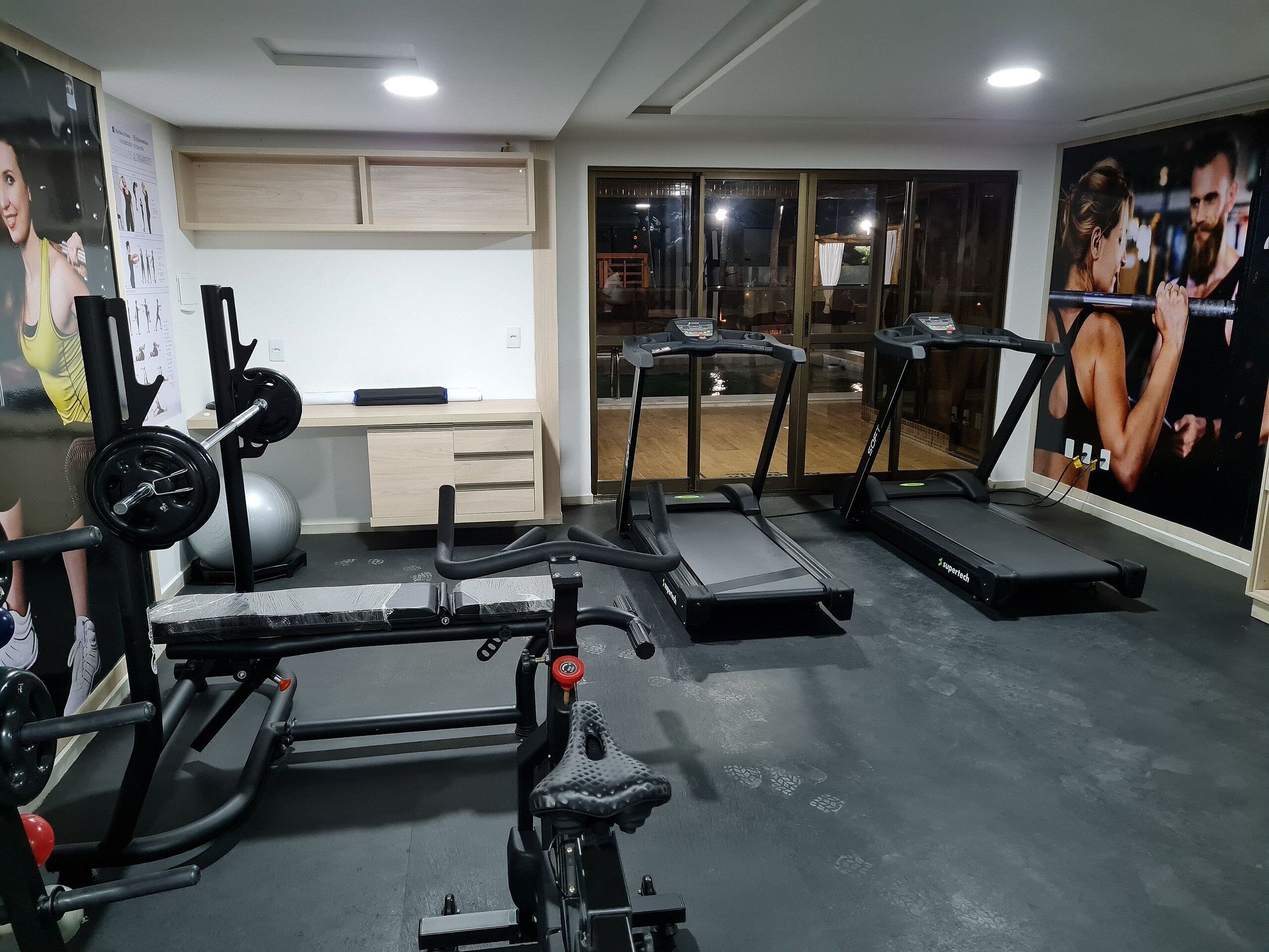 A gym with treadmills, a weight bench, and a wall with fitness posters.