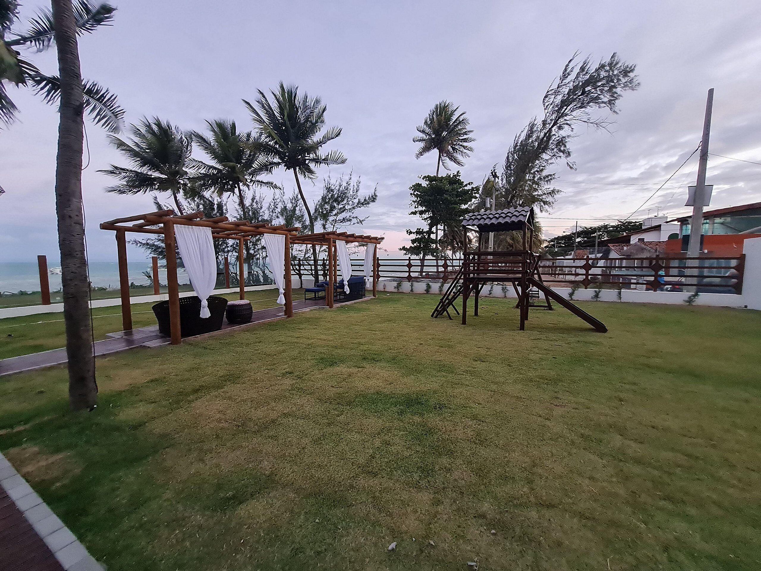 A grassy outdoor area with a wooden swing set and a covered seating area.