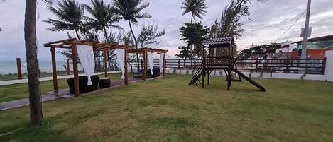 A grassy outdoor area with a wooden swing set and a covered seating area.