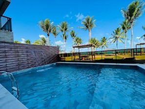 A swimming pool with a geometric wall design, surrounded by palm trees and a clear blue sky. - Amaranth Beach Class (Cabedelo)