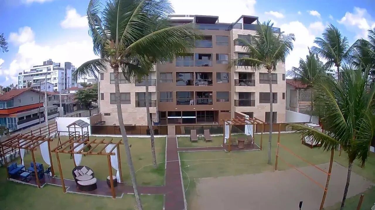A multi-story building with balconies, a playground with swings and a slide, and palm trees.