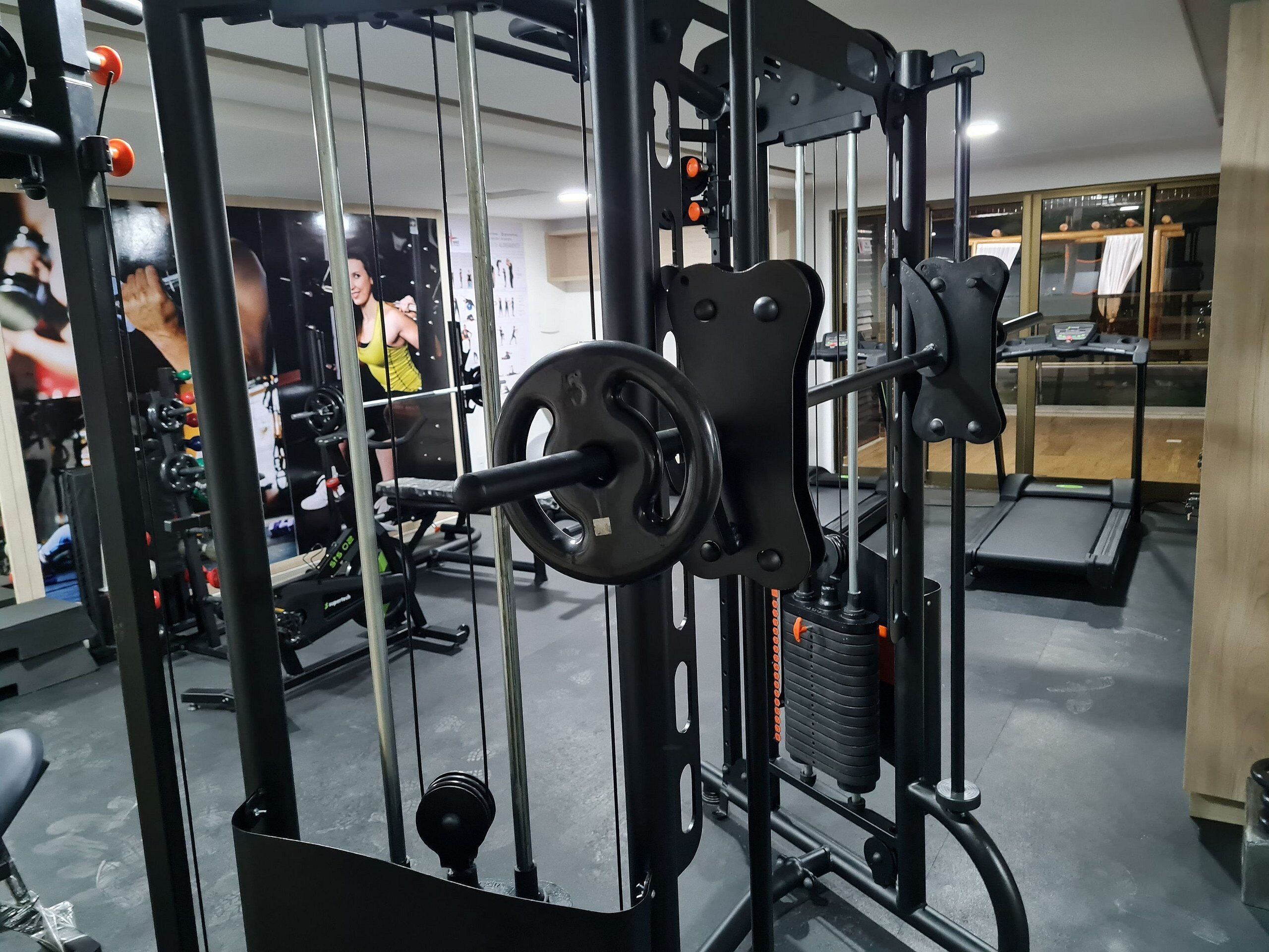 Un gimnasio con equipo de ejercicio, cinta de correr y un espejo que refleja a una persona entrenando.