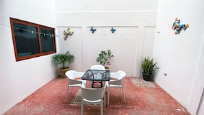 Eine kleine Terrasse mit Tisch und Stühlen, Blumentöpfen und einem Fenster mit Vorhang.